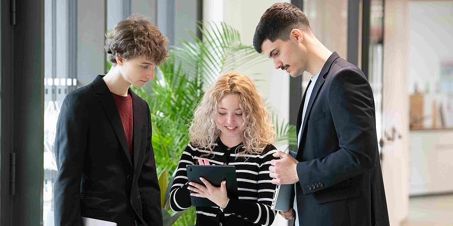 Three students look at a tablet computer while chatting.