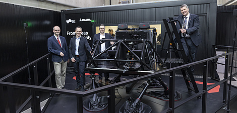 Four men pose for the camera in front of a cockpit standing on six stilts.