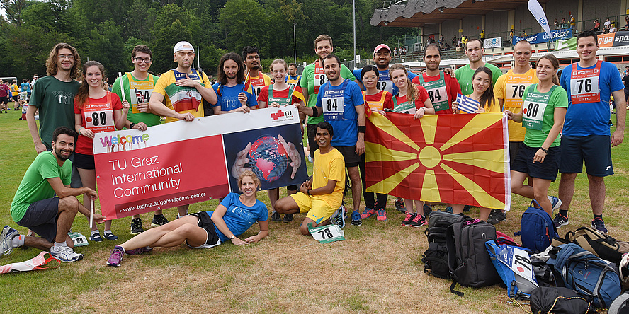 The international TU Graz team wearing blue, green, yellow and red shirts showing the banner „TU Graz International Community“.