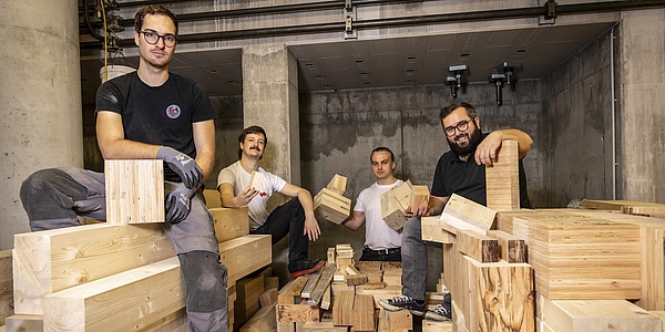 Four men stand and sit on wooden beams.