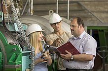 Two men and a woman with helmets and heavy chains and machine parts.