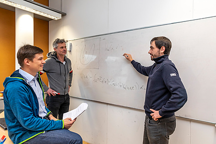 Three researchers in conversation in front of a whiteboard
