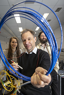 Three people look through a loop of glass fiber