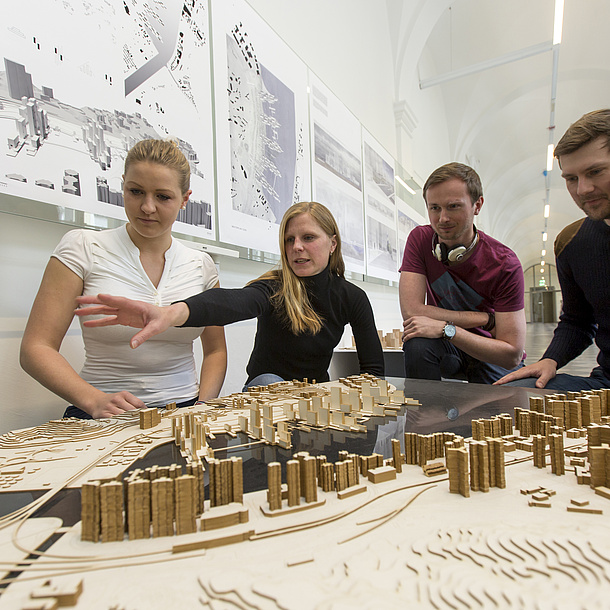 Frauen und Männer stehen an einem Tisch mit Architektur-Modellen.