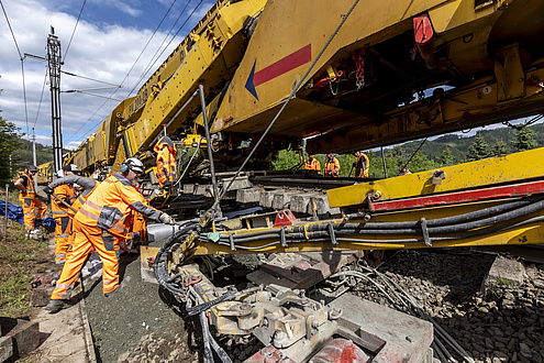Large construction vehicle on rails, debris and men in safety clothing and helmets.