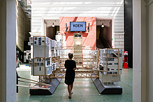 A woman looks at large building models made of wood and paper.