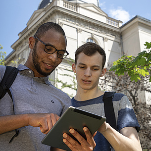Two young men with a tablet in front of a building.