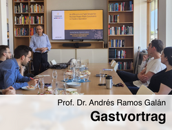 Prof. Dr. Andrés Ramos Galán hält einen Gastvortrag zum Thema flexible Betriebsführung von Kernkraftwerken vor einer kleinen Gruppe von Zuhörer:innen in einem Besprechungsraum mit Bücherregalen und Präsentationsbildschirm.