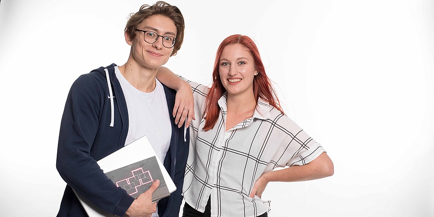 Young woman with her elbow on the shoulder of a young man with a notebook, both standing