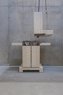 A piece of wood on a rope is lowered onto two joined pieces of wood below.