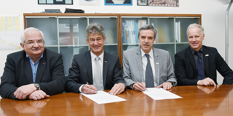Vier Herren bei der Vertragsunterzeichnung an einem Tisch sitzend