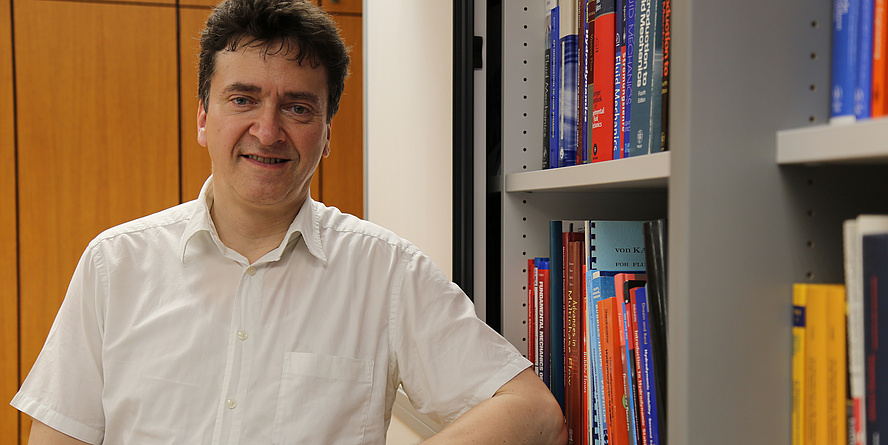 A man in a white shirt stands next to a colourful bookshelf.