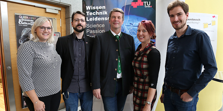 Fair-haired young woman with glasses, dark-haired young man with beard and glasses, greying man in a Styrian jacket, young woman with reddish hair and young man with brown beard in front of a banner bearing the title “Wissen, Technik, Leidenschaft”