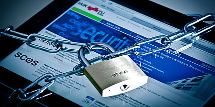A tablet in the background, on which the website of the Institute for Applied Information Processing and Communication Technologies is open, with a chain with padlock in front
