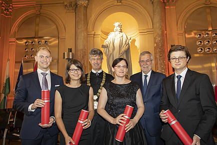 Zwei Frauen und vier Männer stehen nebeneinander, vier von Ihnen halten rote Rollen in der Hand.