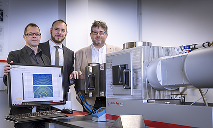 Three researchers grouped around a laboratory instrument