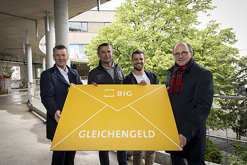 Four men are standing together holding a large envelope in their hands.
