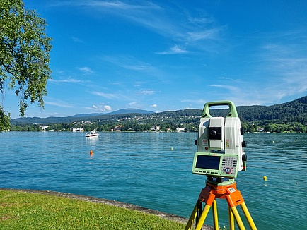 A technical device similar to a camera stands on a tripod at the shore of a lake.