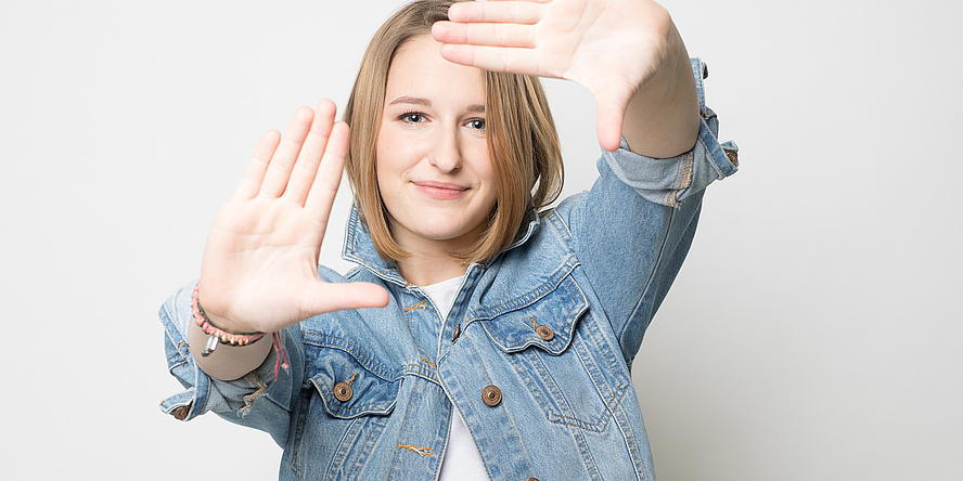 Junge Frau mit blauer Jeansjacke und weißem Shirt streckt ihre Hände in Richtung Kamera.