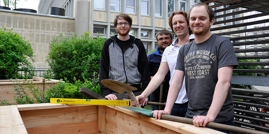 Die vier Helfer, die die Hochbeete aufgebaut haben, lachen mit Gartenwerkzeugen in der Hand in die Kamera.