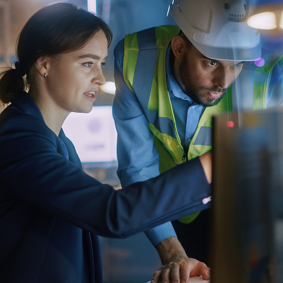 Two people in front of a screen, one person with construction helmet and high-visibility vest