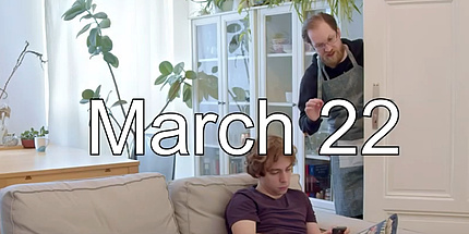 Zwei junge Männer in einem Wohnzimmer, im Bild der Schriftzug "March 22".