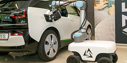 Ein Auto mit offenem Tankdeckel, daneben ein Roboterarm
