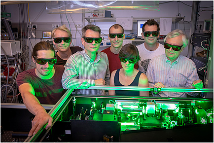 A group of researchers in the physics laboratory bathed in green light