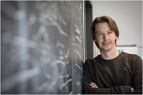 A man stands next to a blackboard.