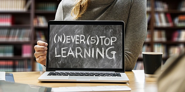 Der Bildschirm eines aufgeklappten Laptops ist zu sehen, darauf ist mit Kreide wie auf einer Tafel geschrieben: never stop learning.