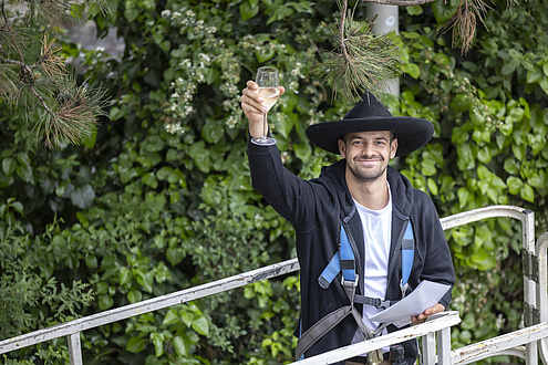 A man in a hat stands on a lifting platform and raises a glass.