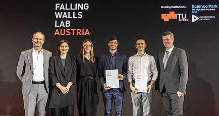 Six people smile into the camera, the second and the third person from the right hold a document saying the have won third place.