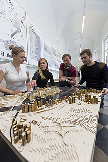 Zwei Frauen und zwei Männer mit einem großen Stadtmodell aus Holz.