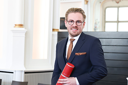 A man holds a red document roll and smiles into the camera.