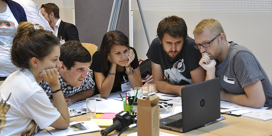 Eine Gruppe von Alpbach Stipendiaten und Stipendiatinnen blicken gemeinsam auf einen Laptop.