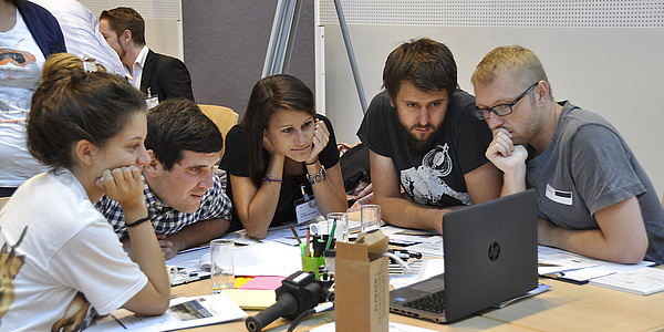 Eine Gruppe von Alpbach Stipendiaten und Stipendiatinnen blicken gemeinsam auf einen Laptop.