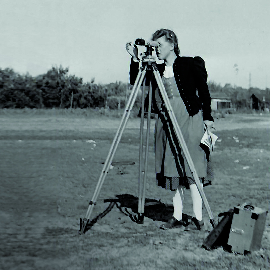 The black and white picture shows a woman at a surveying device.
