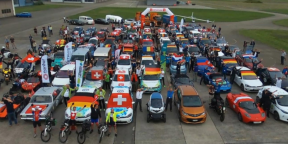 Unzählige Elektromobile von Autos über Bikes bis Scooter stehen auf einem grooßen Platz, teils geschmückt mit den Nationalflaggen der Teams.