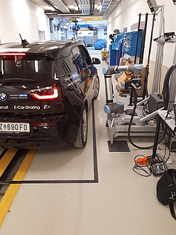 Ein blaues Elektrofahrzeug wird in einer Halle mittels des Roboterladesystems aufgeladen. Man sieht, dass das Fahrzeug eine nicht exakte Parkposition einnimmt.