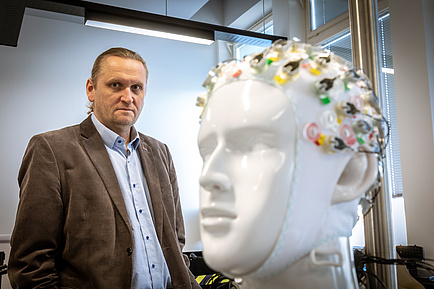 Mann mit Anzug neben einem Modell eines Kopfes, der eine EEG-Haube trägt