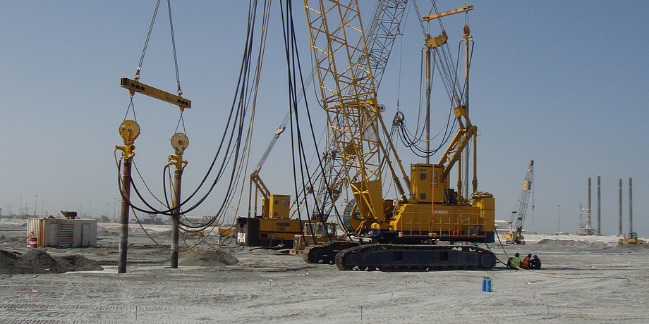 Huge contruction machines stand on desert sand. The soil is worked on. The sky is blue.