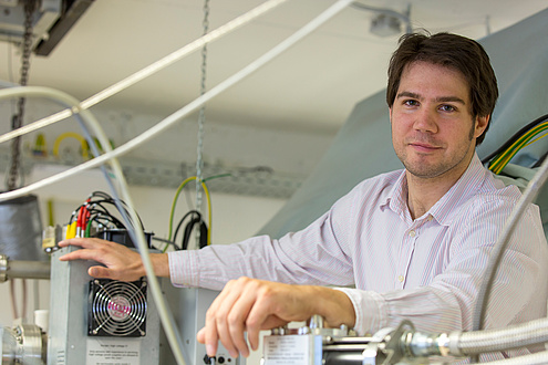 A man in a shirt is standing in front of laboratory equipment. Various cables can be seen. 