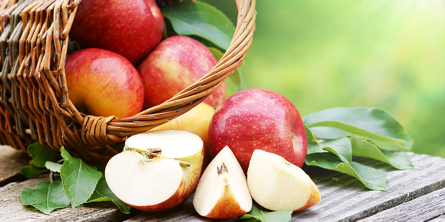 Äpfel im Körbchen liegend auf Holzunterlage mit grünen Blättern 