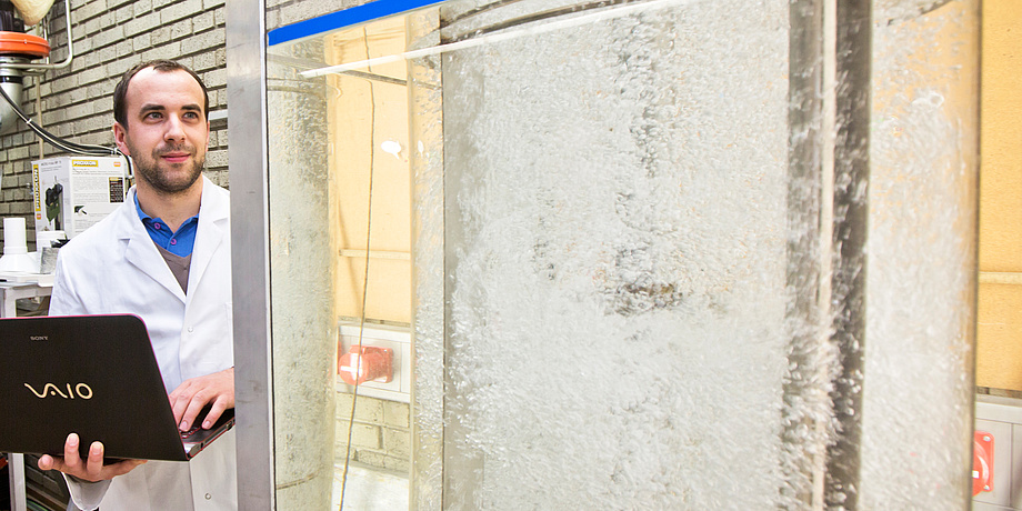 A man with computer in front of an oversized plexiglass tube with water