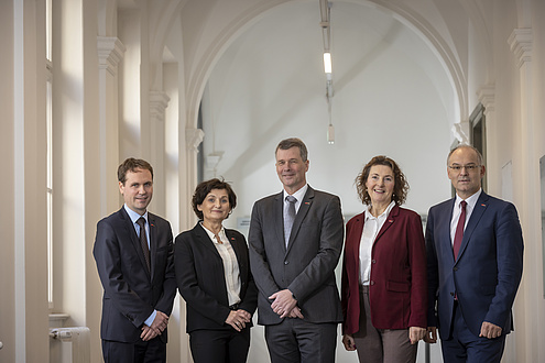 Zwei Frauen und drei Männer freundlich lächelnd in einer Reihe stehend.