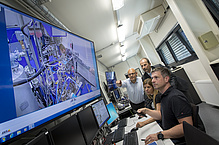 Several people in front of a very large screen showing details of a machine.