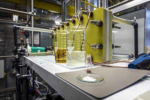Eine Schale mit Pulver, ein kleines Glas mit Pulver und zwei große Gläser mit Flüssigkeit stehen vor einem Versuchsaufbau auf einem Tisch