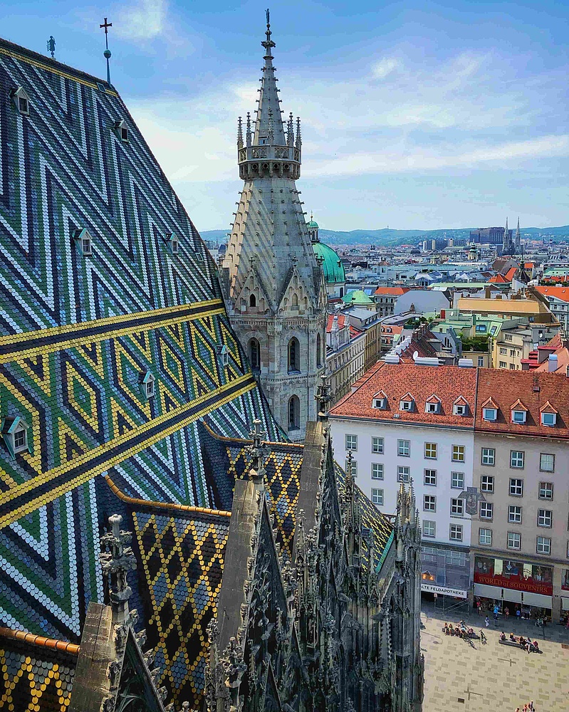 Blick auf das mit Mosaik besetzte Dach einer gotischen Kathedrale und umliegende Häuser.