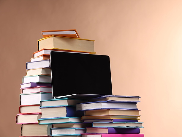 Bücherstapel und ein Laptop, brauner Hintergrund.