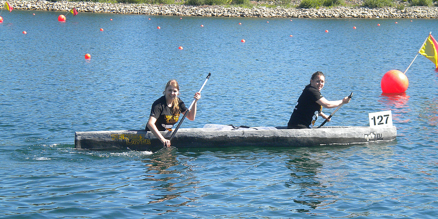 Two woman are sitting in a little grey canoe in the middle of a lake.
